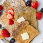 a plate of sliced french toaste with berries, ،er, and maple syrup