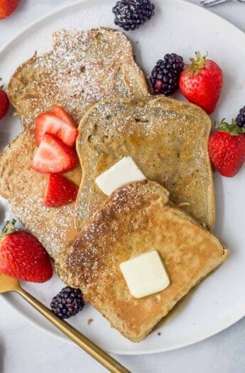 a plate of sliced french toaste with berries, butter, and maple syrup