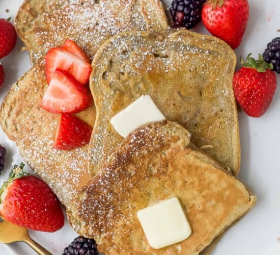 a plate of sliced french toaste with berries, butter, and maple syrup