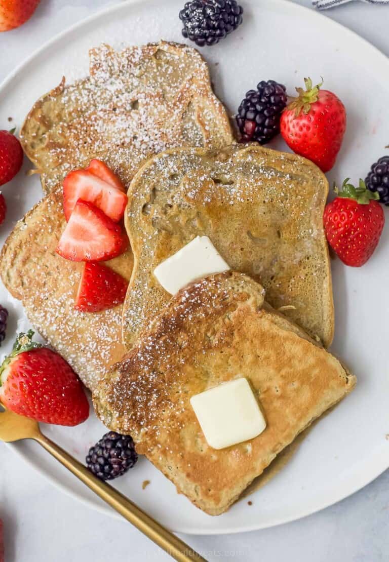 a plate of sliced french toaste with berries, butter, and maple syrup