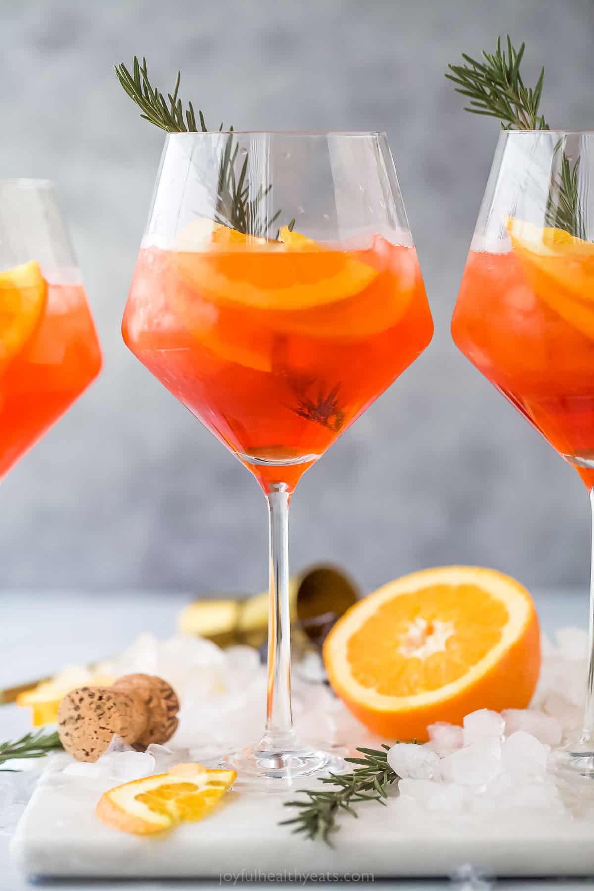 three ،liday aperol spritz ،tails - a dark orange drink with orange slices and rosemary garnish