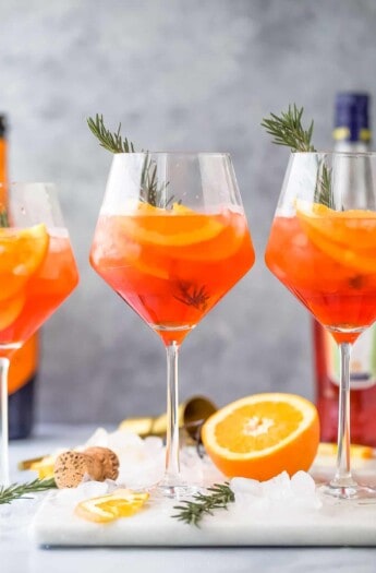 three holiday aperol spritz cocktails - a dark orange drink with orange slices and rosemary garnish