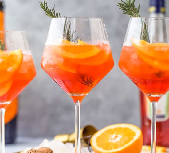 three holiday aperol spritz cocktails - a dark orange drink with orange slices and rosemary garnish
