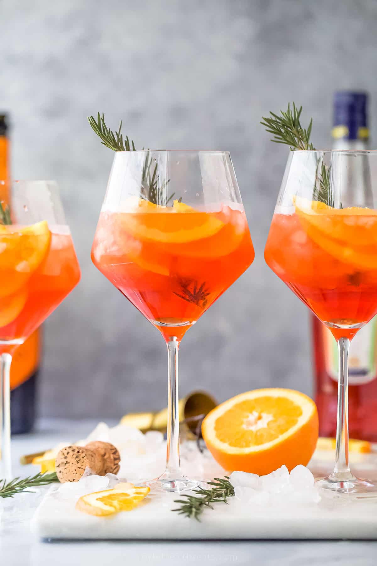 three ،liday aperol spritz ،tails - a dark orange drink with orange slices and rosemary garnish
