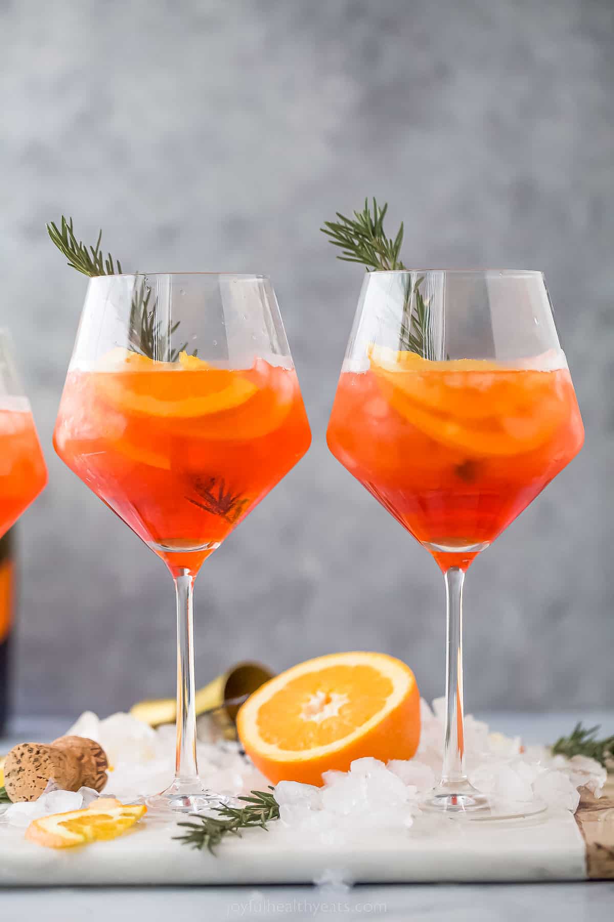 two holiday aperol spritz cocktails - a dark orange drink with orange slices and rosemary garnish