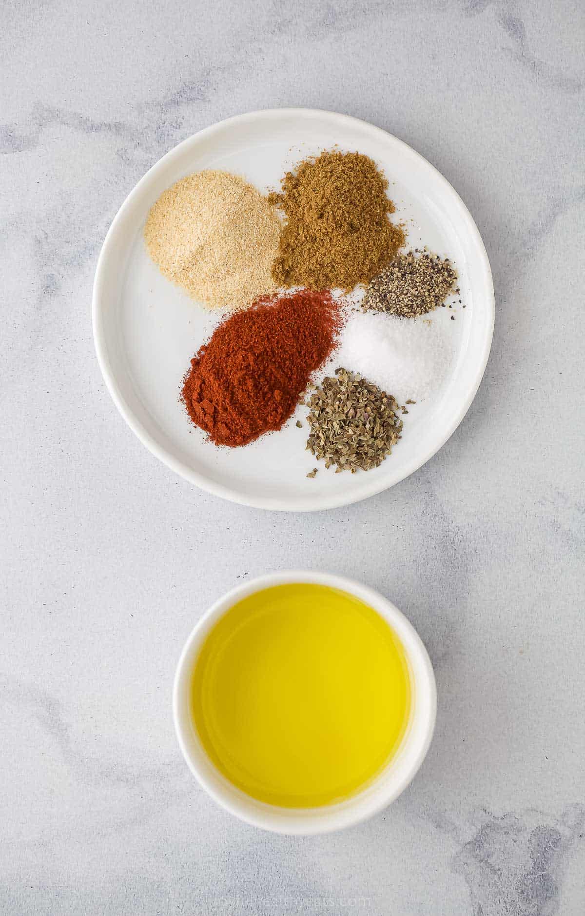 a small bowl with olive oil and plate with seasonings