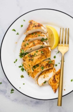 slice chicken breast on a plate with parsley garnish and lemon