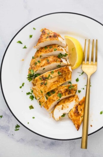 slice chicken breast on a plate with parsley garnish and lemon