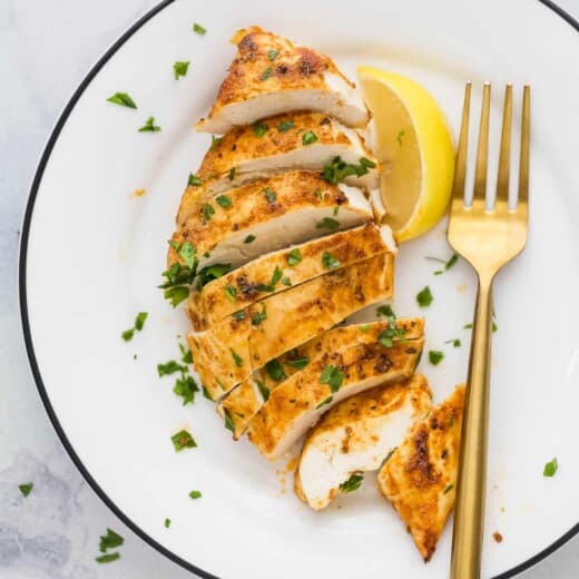 slice chicken breast on a plate with parsley garnish and lemon