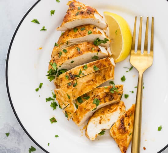 slice chicken breast on a plate with parsley garnish and lemon