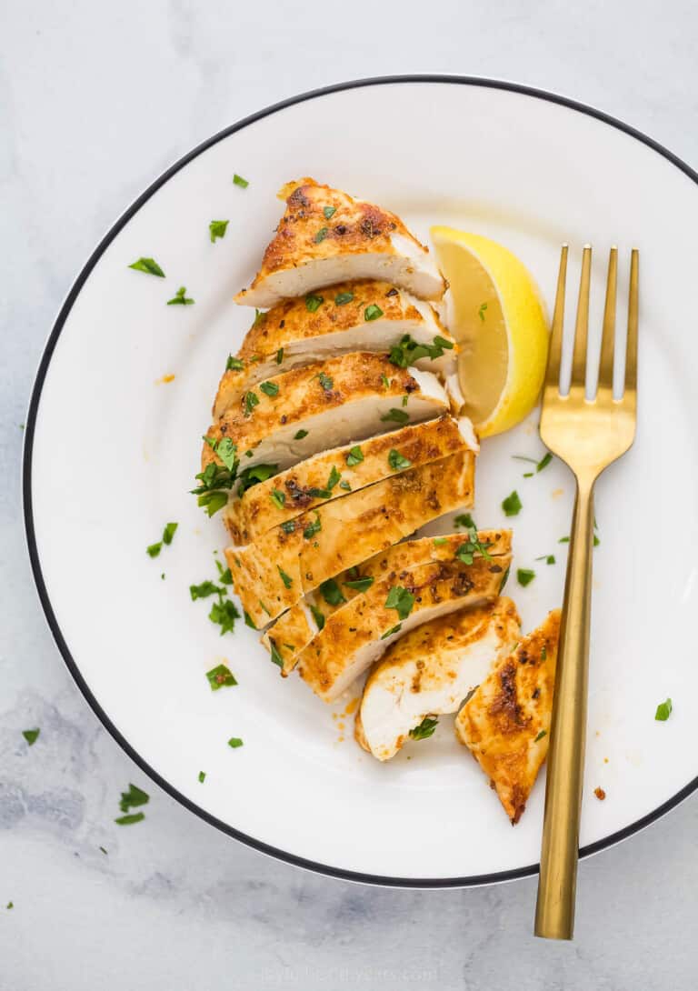 cooked chicken breast sliced on a white plate with a gold fork