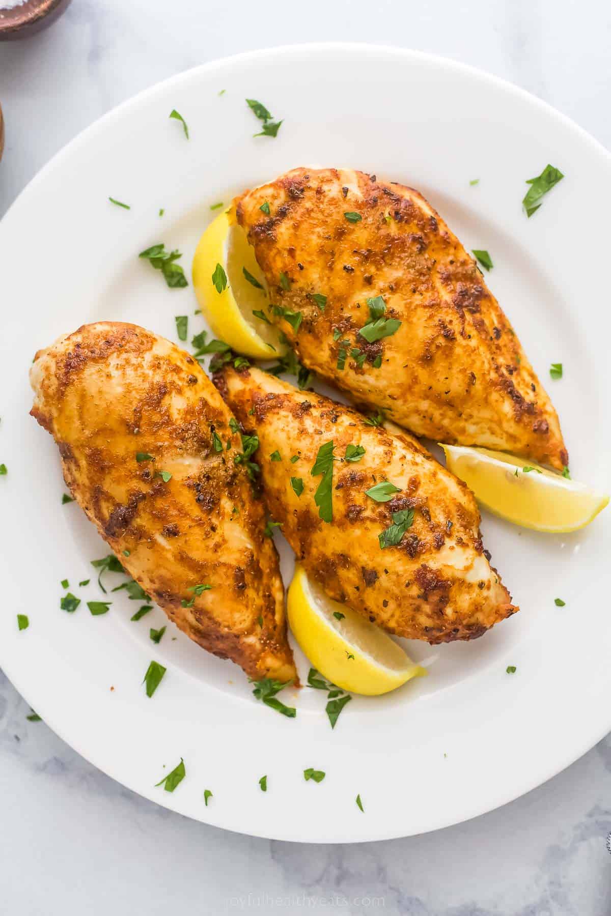 chicken breasts on a plate with parsley garnish and lemon