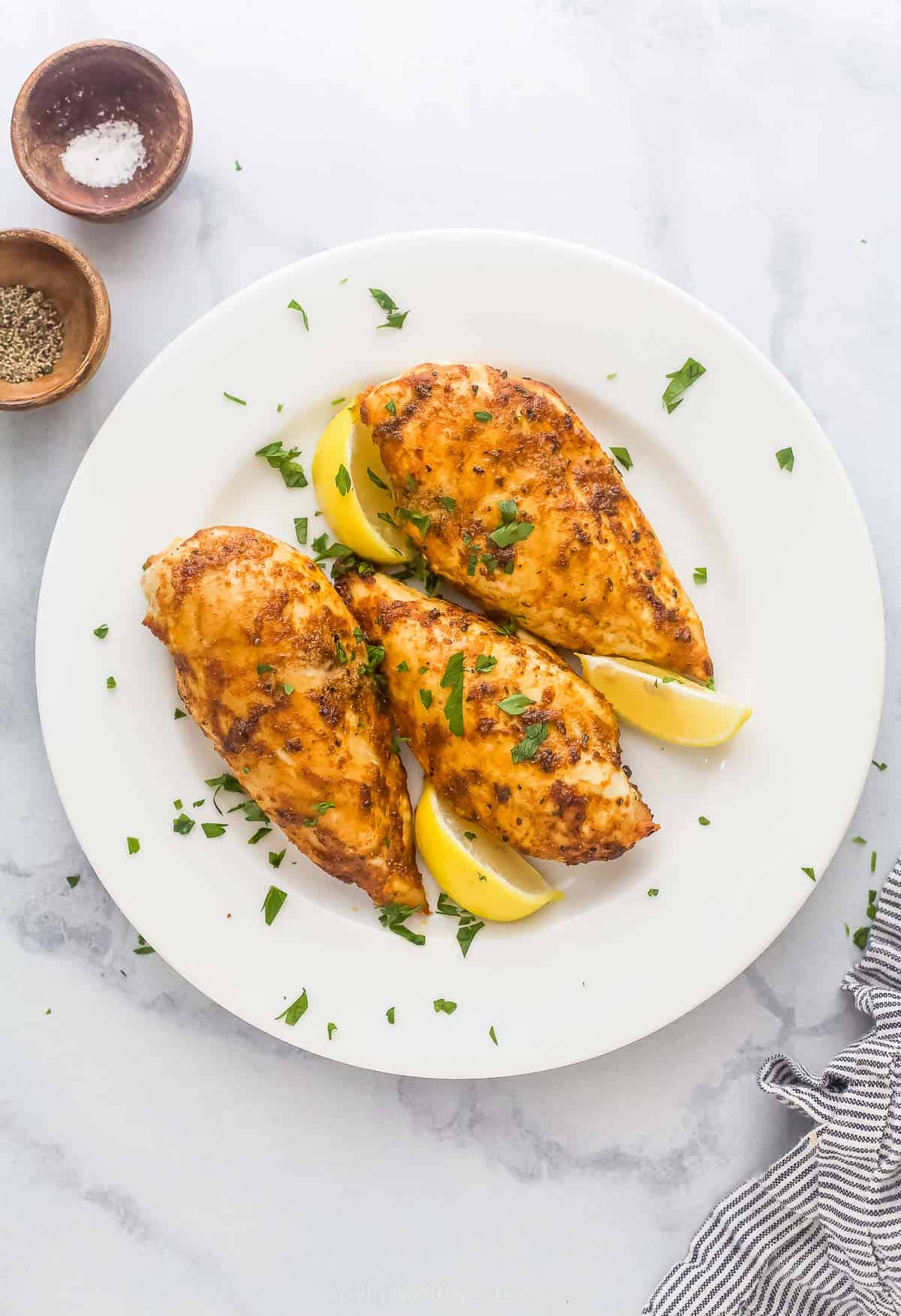 chicken breasts on a plate with parsley garnish and lemon