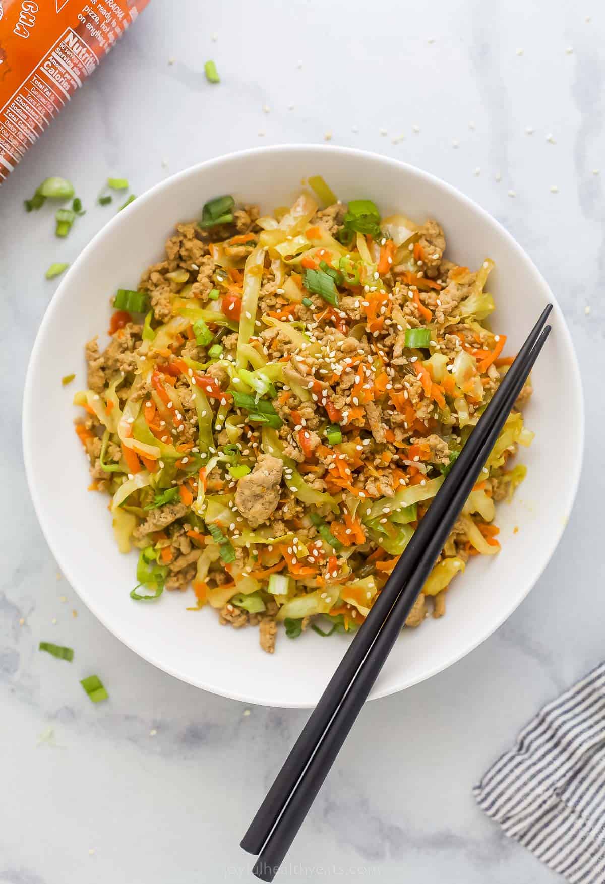 egg roll in a bowl plated in a white bowl which is ground turkey, cabbage, and carrots tossed a soy-based sauce