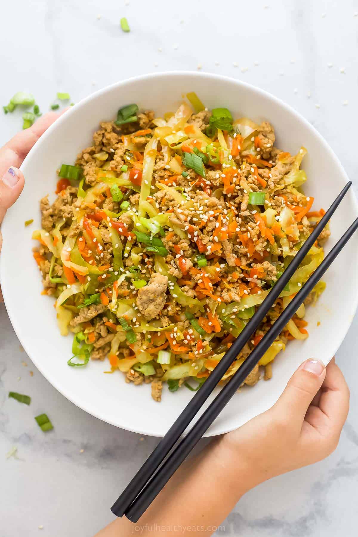 egg roll in a bowl plated in a white bowl which is ground turkey, cabbage, and carrots tossed a soy-based sauce