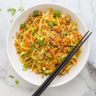 egg roll in a bowl plated in a white bowl which is ground turkey, cabbage, and carrots tossed a soy-based sauce