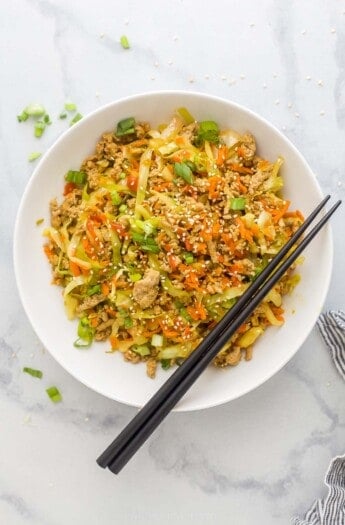 egg roll in a bowl plated in a white bowl which is ground turkey, cabbage, and carrots tossed a soy-based sauce