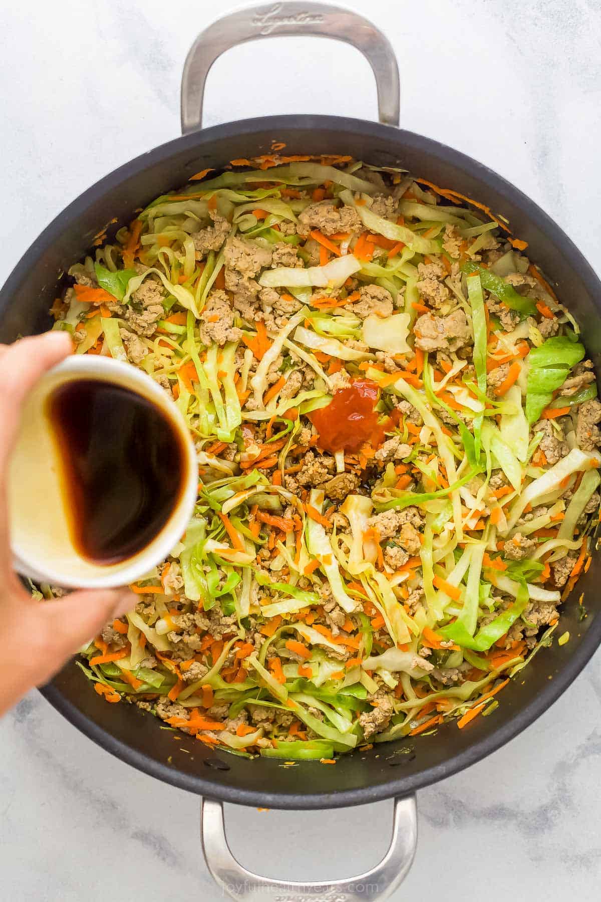 pouring sauce into a pan to make egg roll in a bowl out of ground turkey, cabbage, and carrots