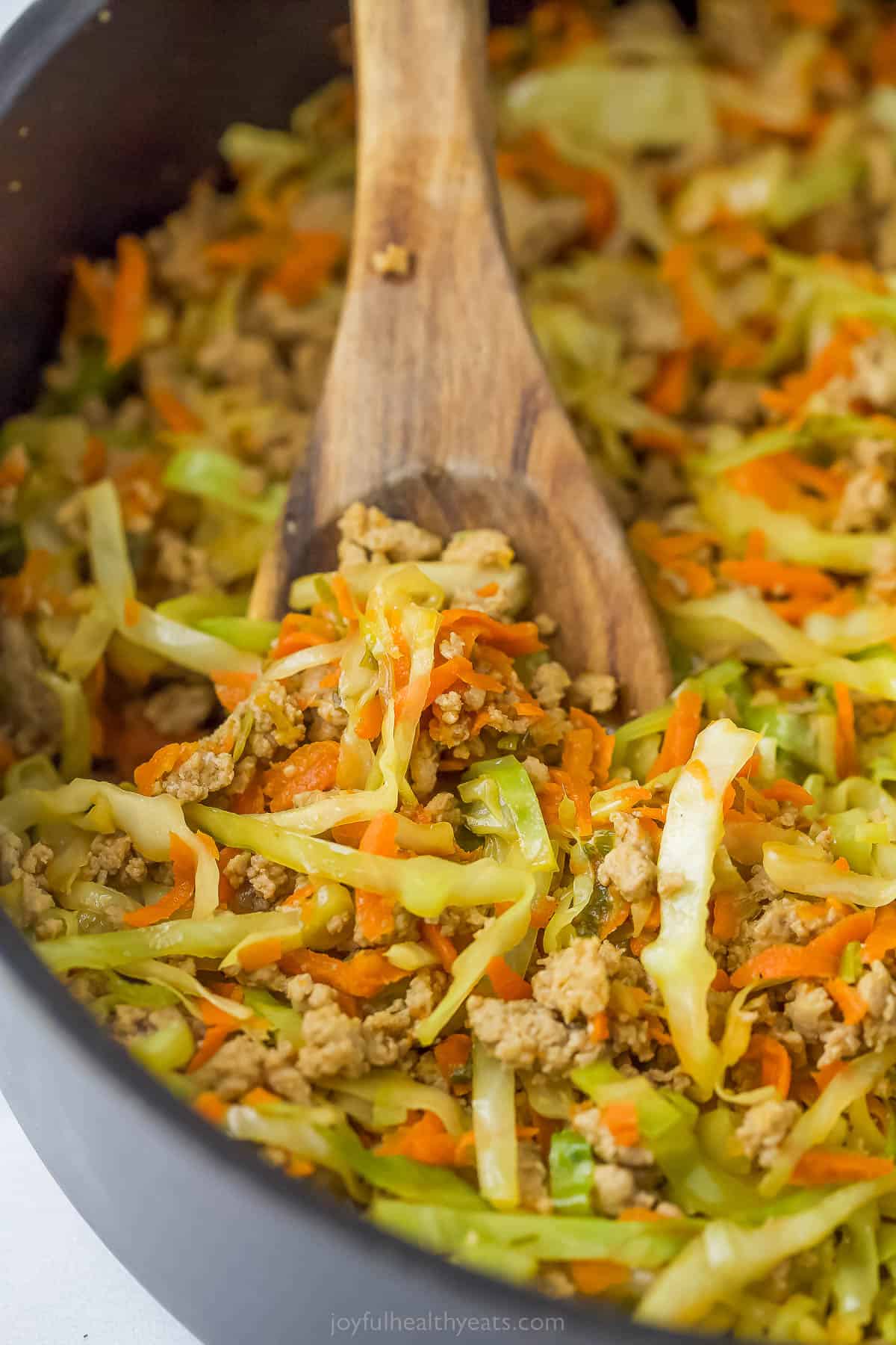 a wooden s، in a pan with cabbage, carrots, and ground turkey