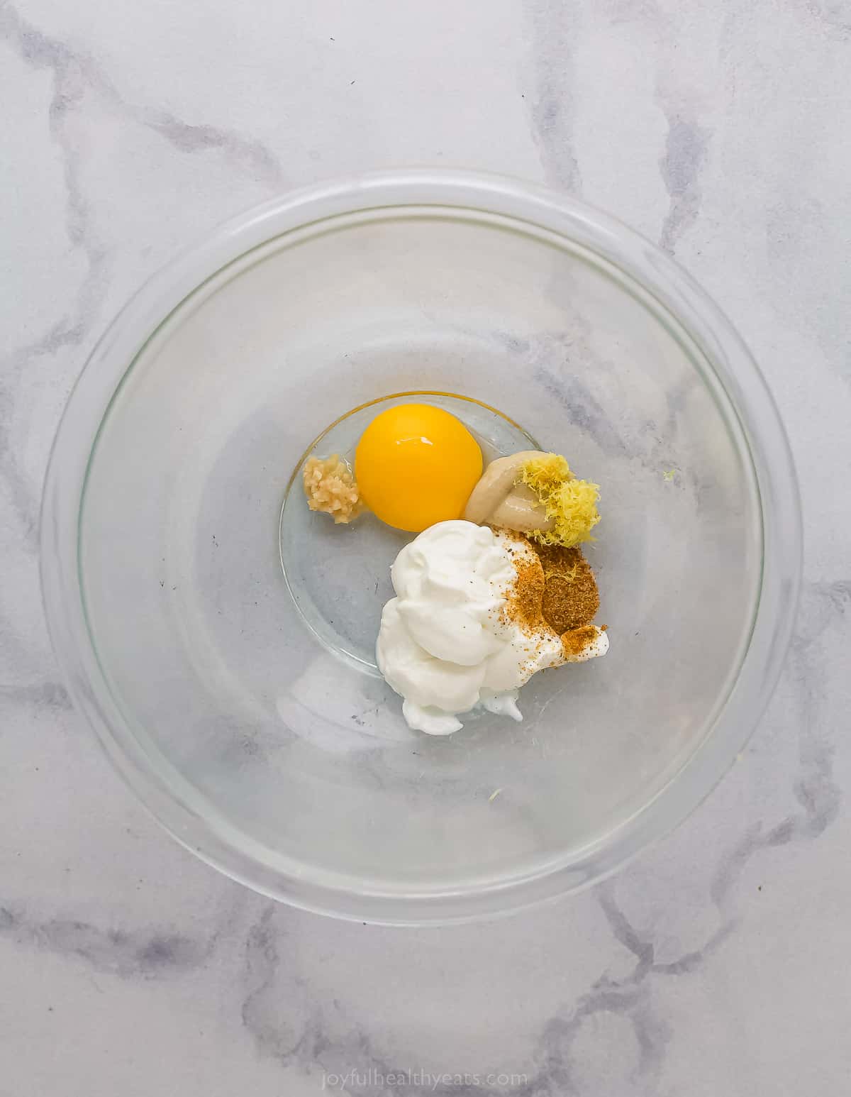 a bowl with an egg yolk, yogurt, mus،, old bay and garlic
