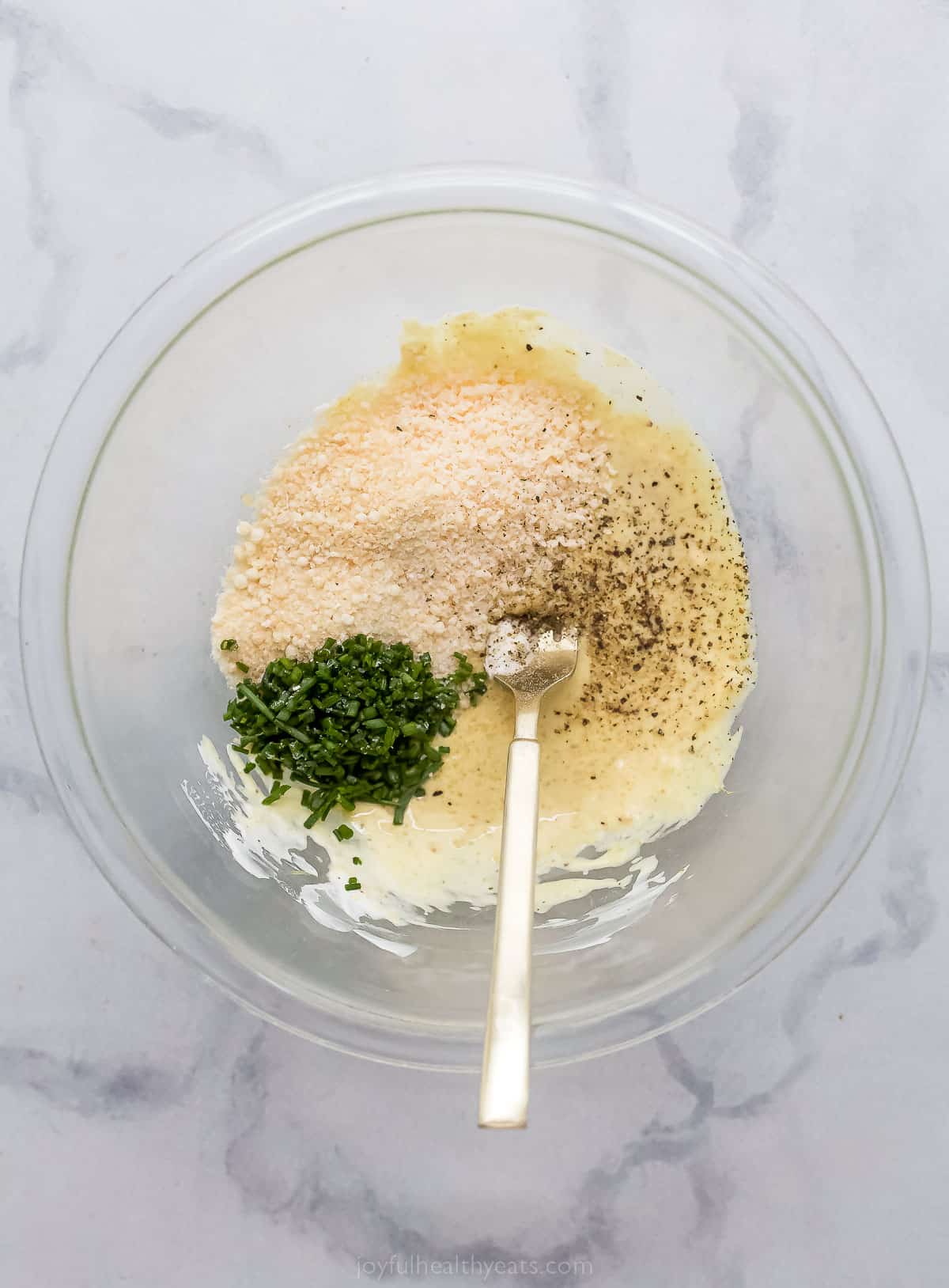 a bowl with bread c،bs, herbs, and parmesan cheese being mixed into a yogurt mixture