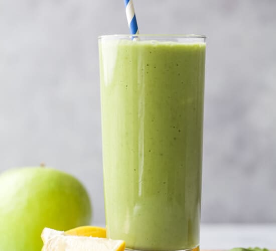 green detox smoothie in a tall glass with straw