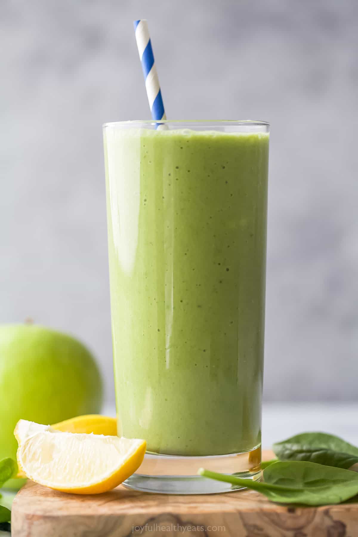 green detox smoothie in a tall glass with straw