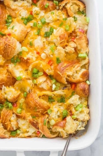 croissant breakfast casserole with eggs, cheese, peppers, green onions, and cheese in a white ceramic dish