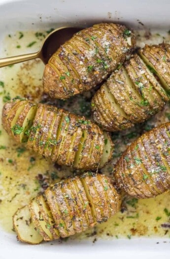 whole potatoes with thin slices with garlic and herbs on top in a baking dish