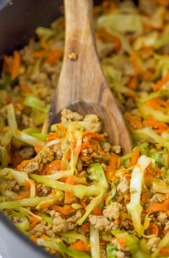 a wooden spoon in a pan with cabbage, carrots, and ground turkey