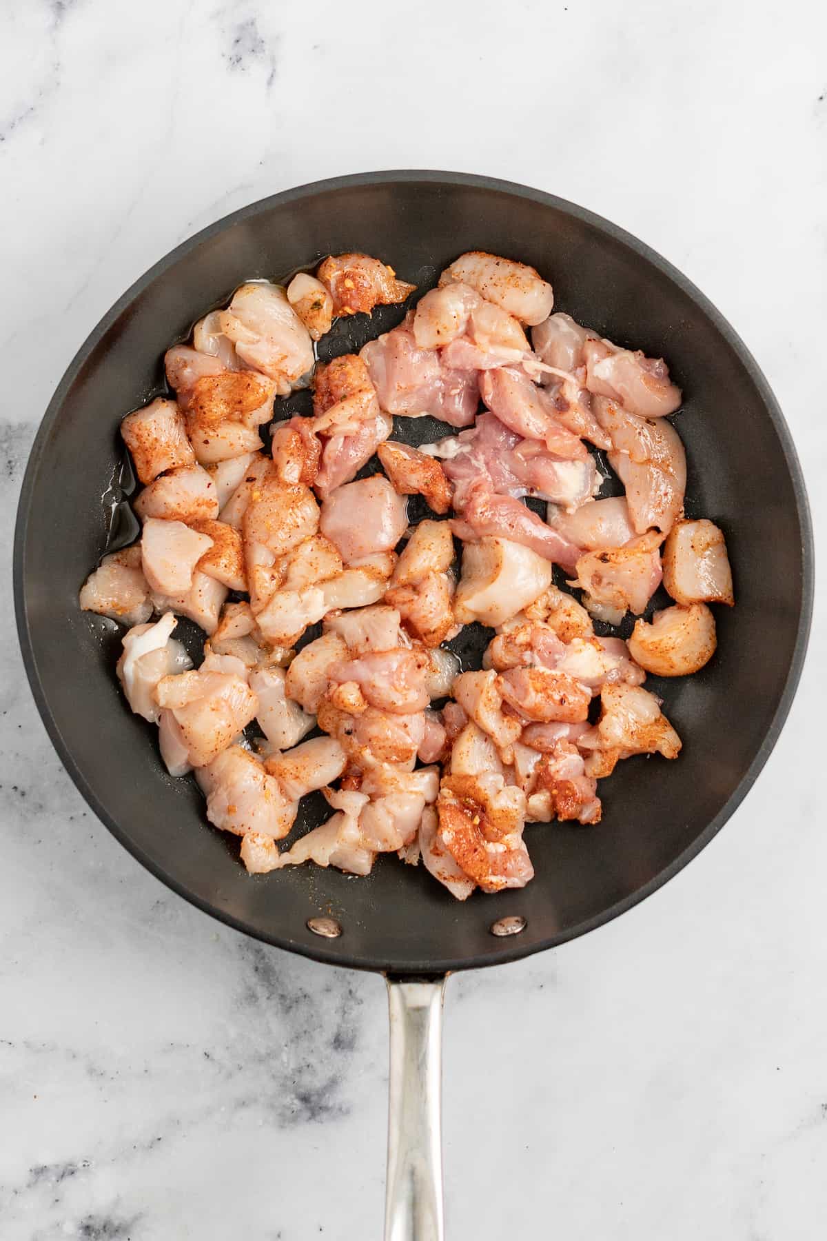 cooking bites of chicken in a saute pan that have been seasoned with spices