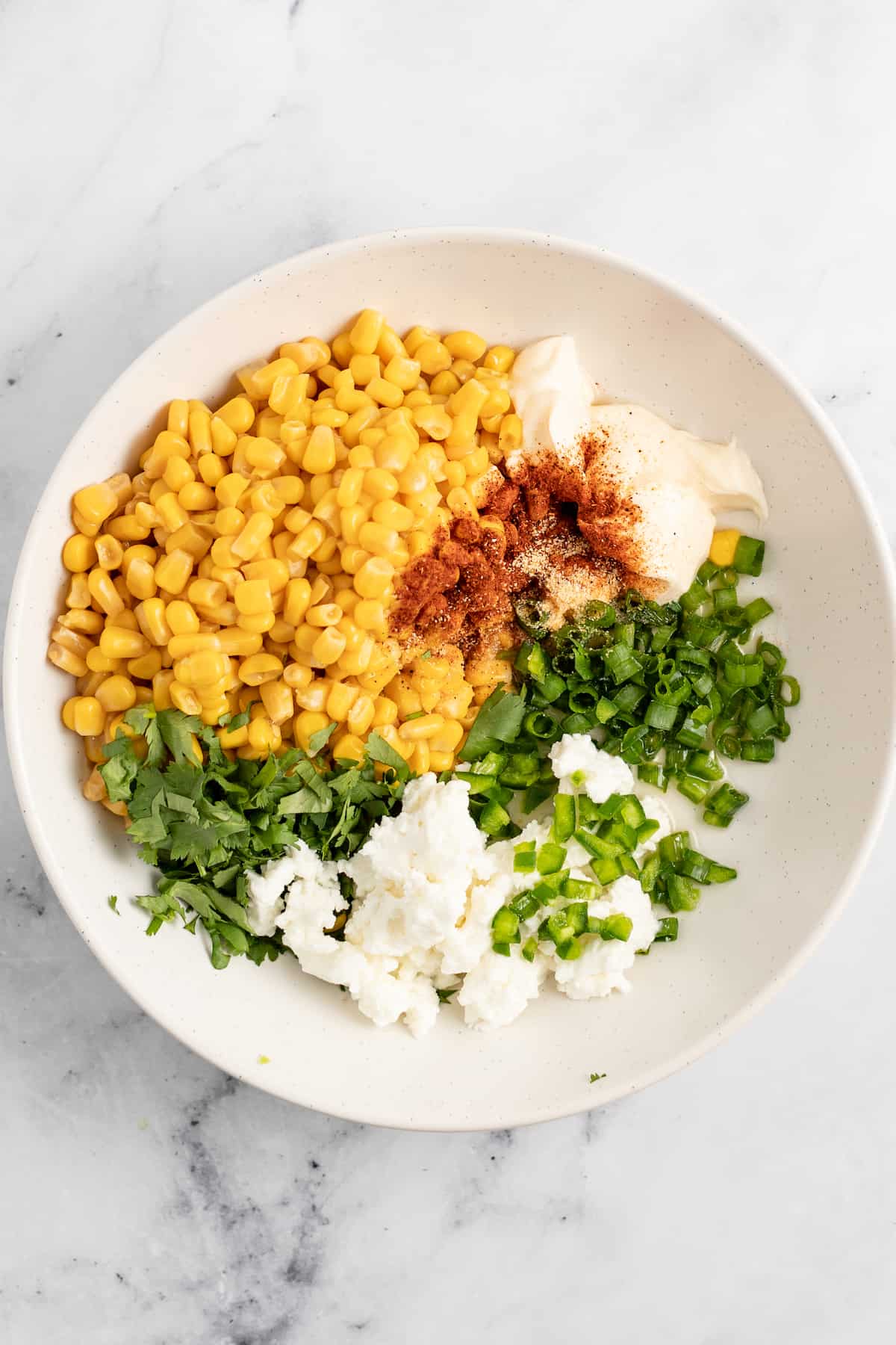 ingredients in a bowl to make a corn salad like corn, herbs, mayo, and green onions