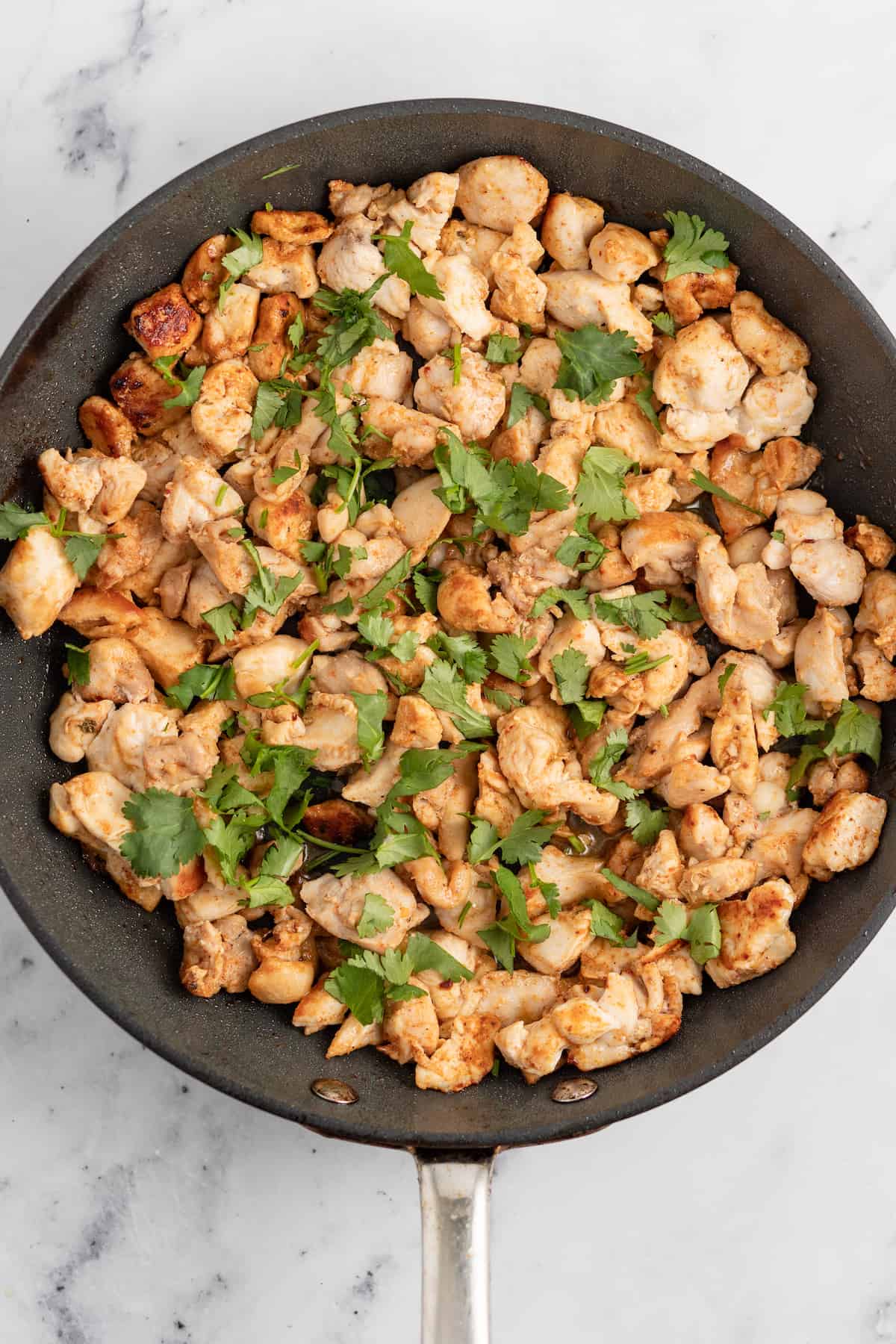 cooked seasoned chicken in a pan garnished with fresh herbs