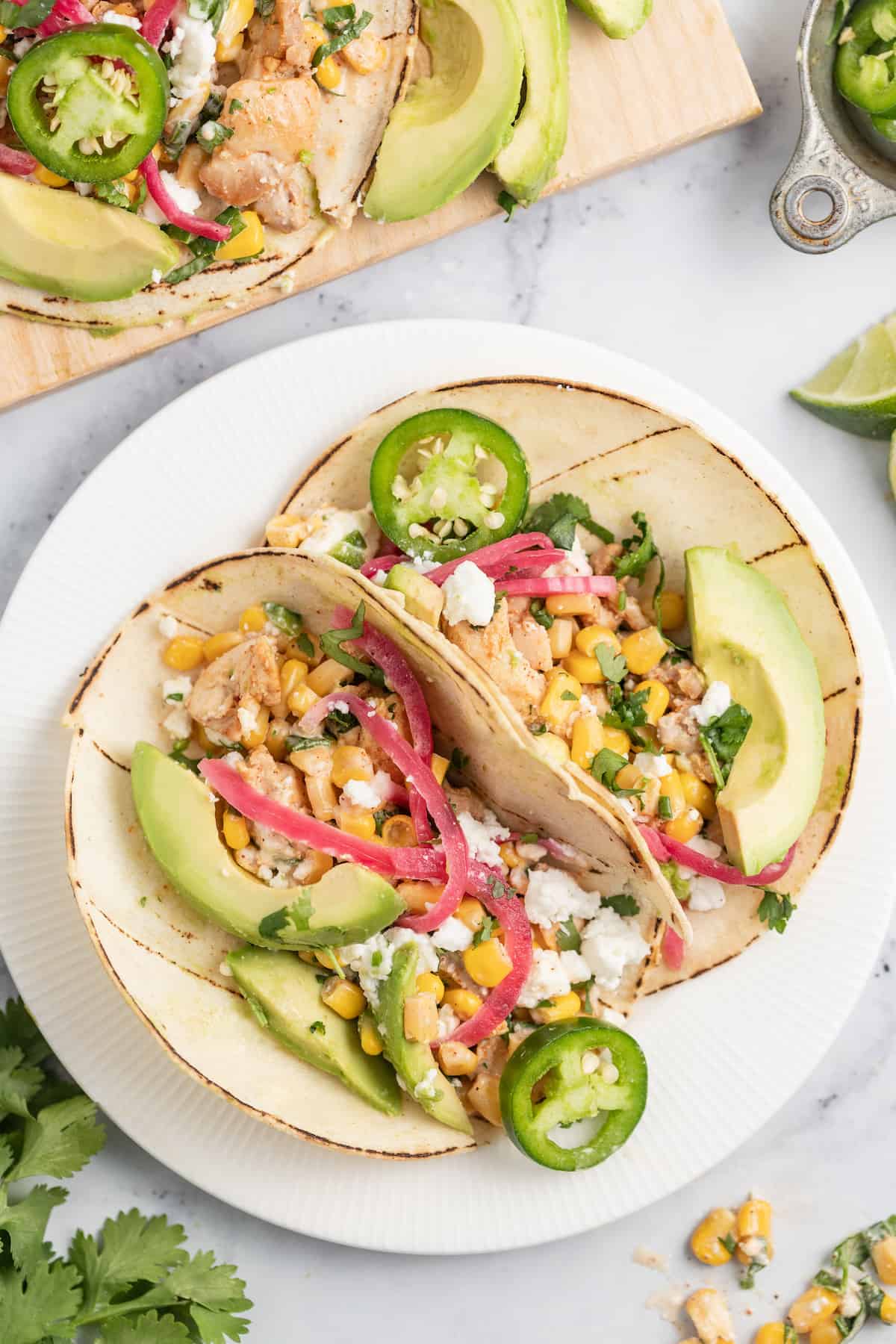 two plated Chicken Street Tacos with avocado, pickled onions, and corn salad