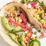 two plated Chicken Street Tacos with avocado, pickled onions, and corn salad