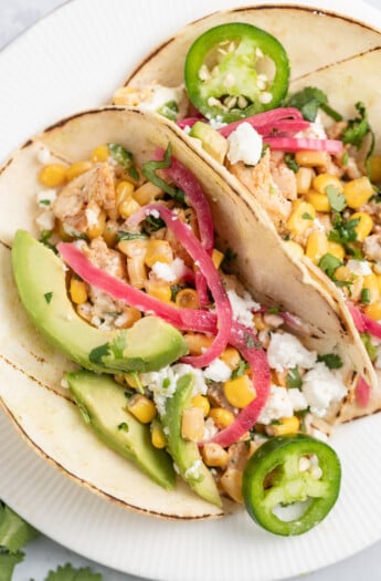 two plated Chicken Street Tacos with avocado, pickled onions, and corn salad