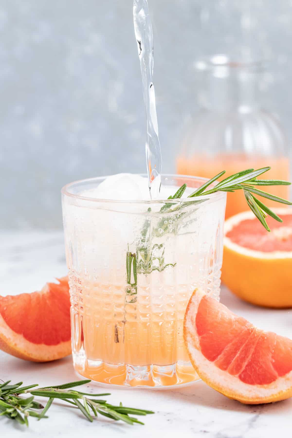 pouring sparkling water into a low ball glass that has grapefruit juice in it and ice