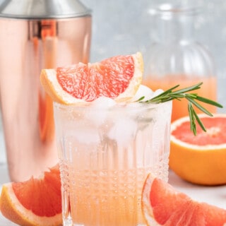 greyhound cocktail made with grapefruit juice and sparking water in a low ball glass with a cocktail shaker behind it