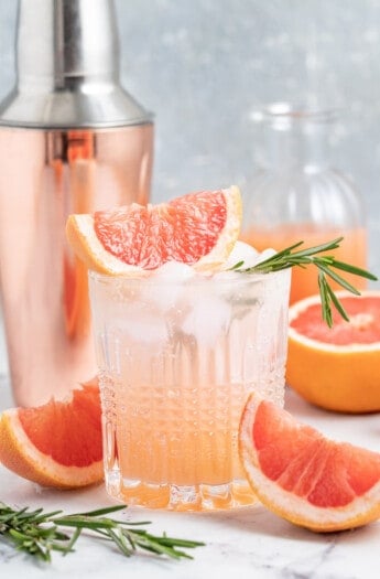greyhound cocktail made with grapefruit juice and sparking water in a low ball glass with a cocktail shaker behind it