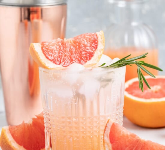 greyhound cocktail made with grapefruit juice and sparking water in a low ball glass with a cocktail shaker behind it