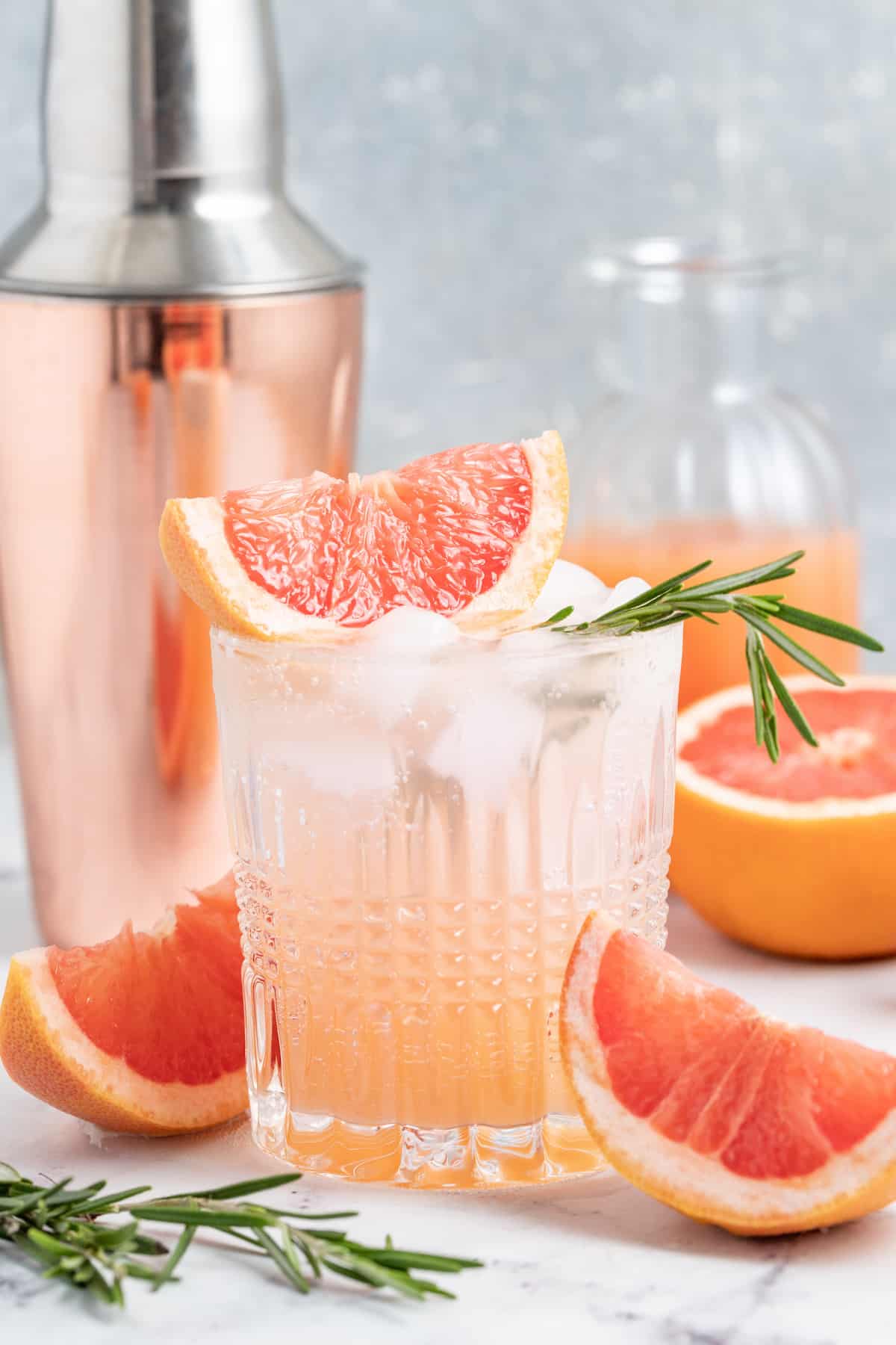 greyhound cocktail made with grapefruit juice and sparking water in a low ball glass with a cocktail shaker behind it