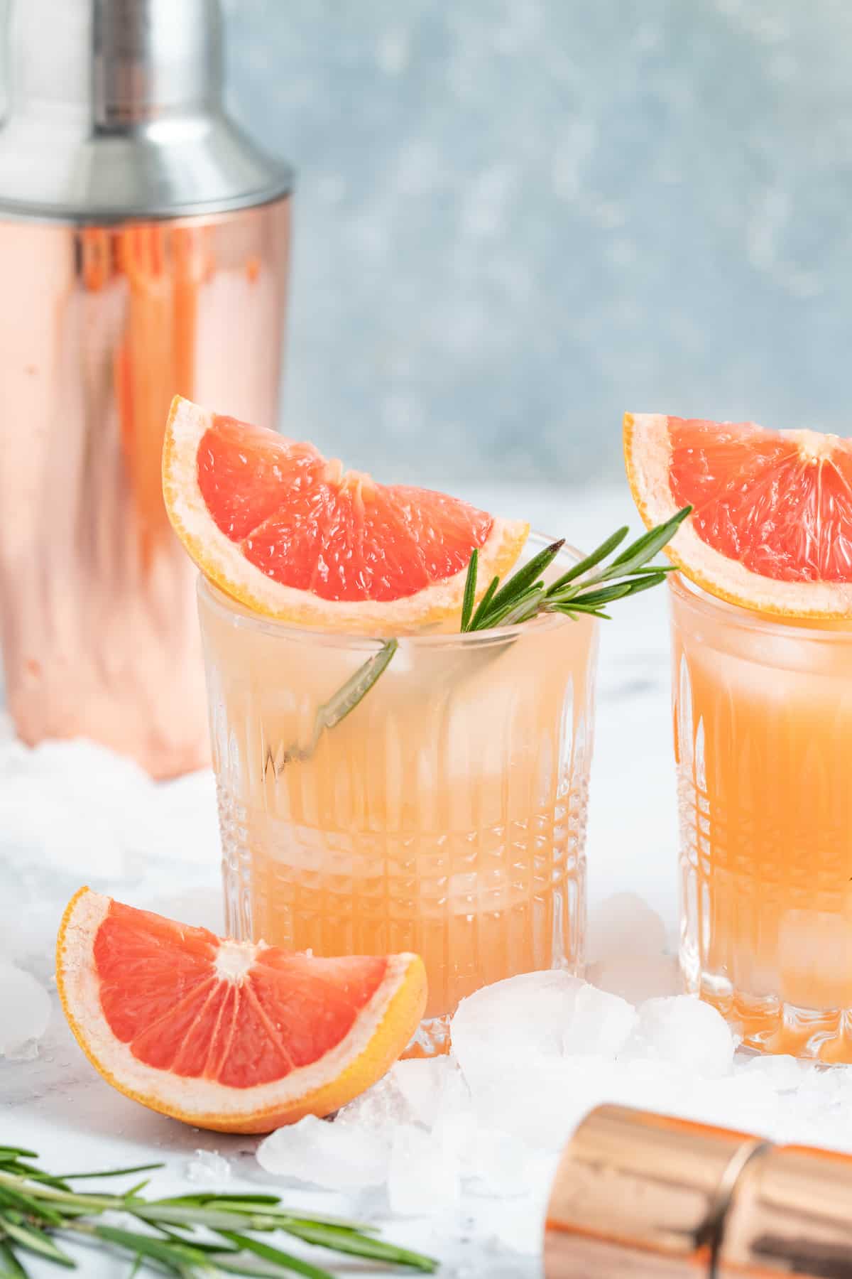 a pale pink beverage known as a greyhiound cocktail in a lowball glass with grapefruit wedge and fresh herb garnish