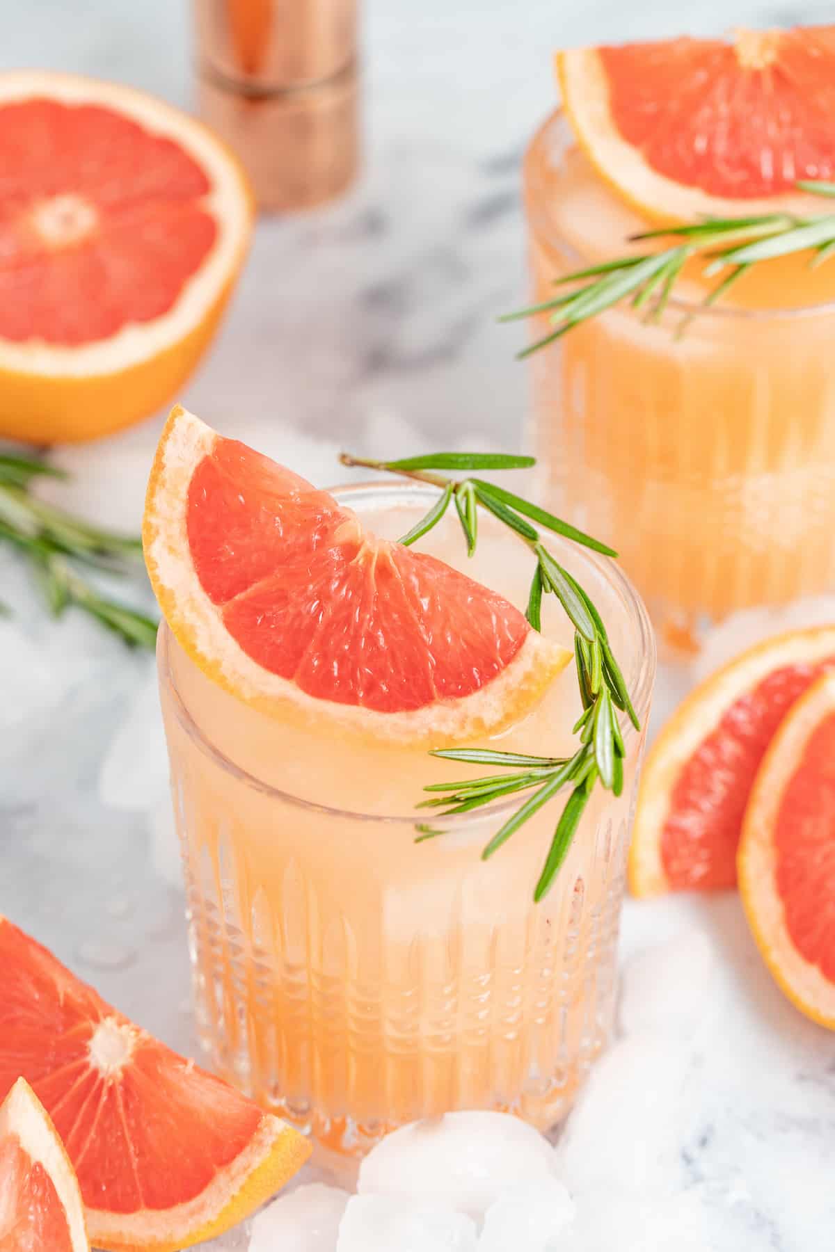 a pale pink beverage known as a greyhiound cocktail in a lowball glass with grapefruit wedge and fresh herb garnish