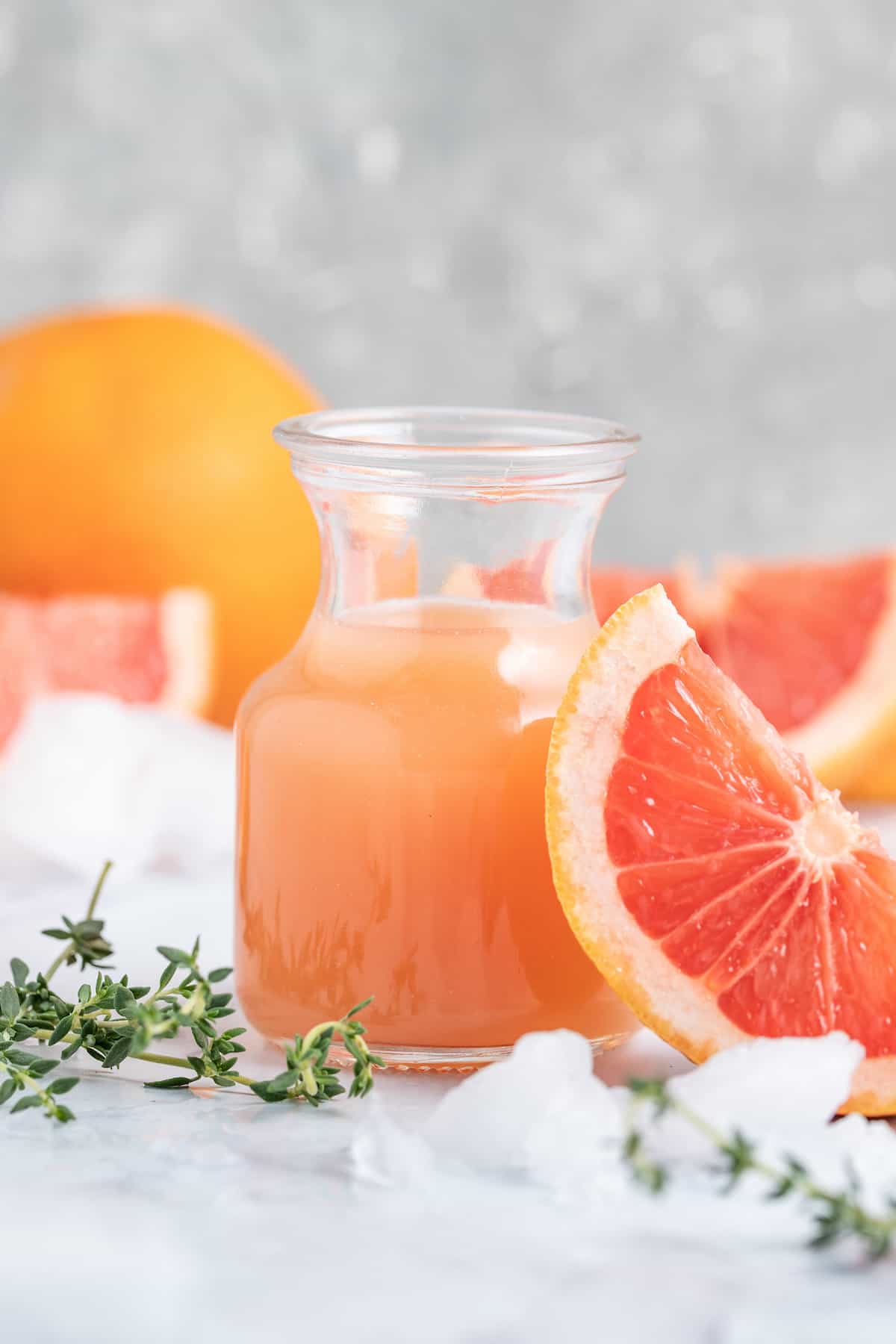 a small karafe of fresh grapefruit juice next to fresh herbs and grapefruit wedge