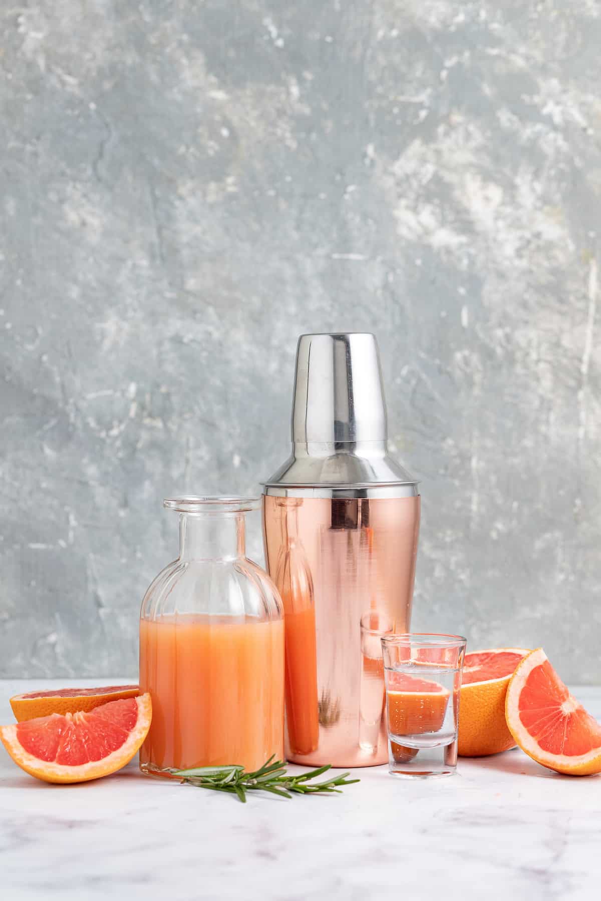 a display of cocktail making ingredients to make a greyhound which includes grapefruit juice, fresh grapefruit, and a cocktail shaker