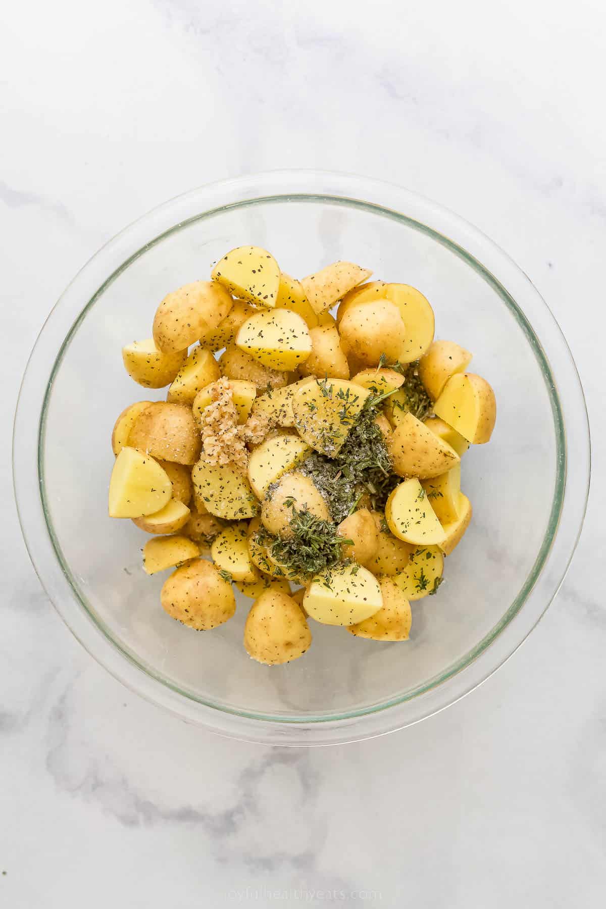 These are the best Air Fryer Roasted Potatoes! Tender on the inside and crispy on the outside. These potatoes are herby and delicious. a glass bowl with potatoes and seasonings