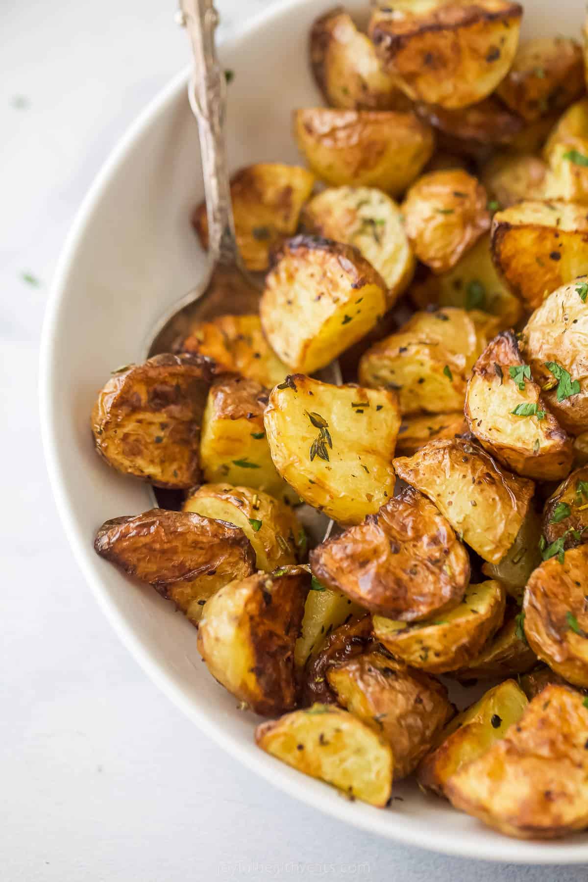 These are the best Air Fryer Roasted Potatoes! Tender on the inside and crispy on the outside. These potatoes are herby and delicious. a bowl of air fryer roasted potatoes