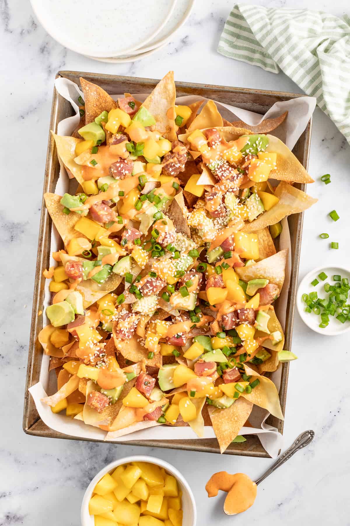 Ahi Tuna Poke Nachos are a unique shareable snack. They are made with homemade wonton chips, seasoned ahi tuna, mango, and avocado. a platter of wonton chips topped with diced ahi tuna, mango, scallions, and sriracha mayo