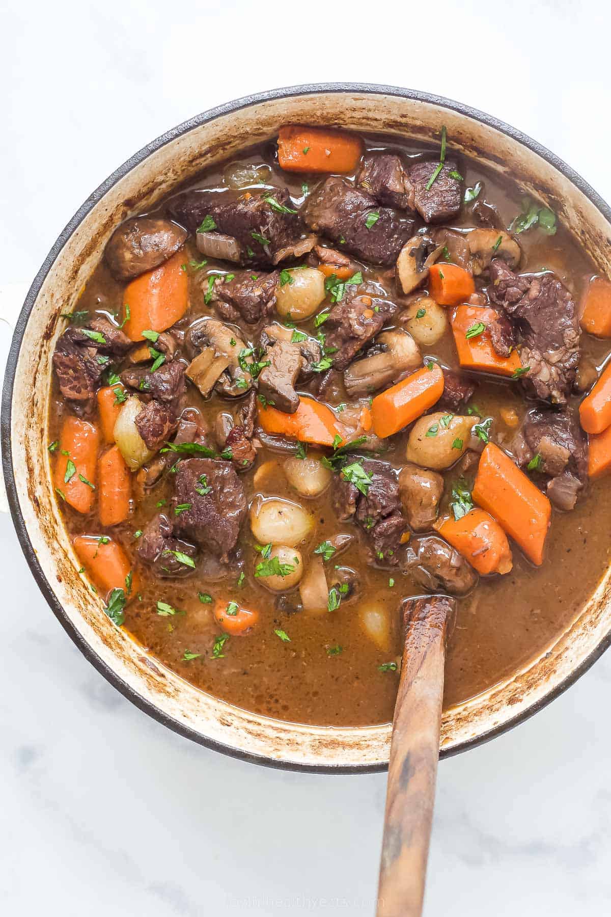 a pot of beef bourguignon with carrots, pearl onions, and mushrooms in a dark gravy