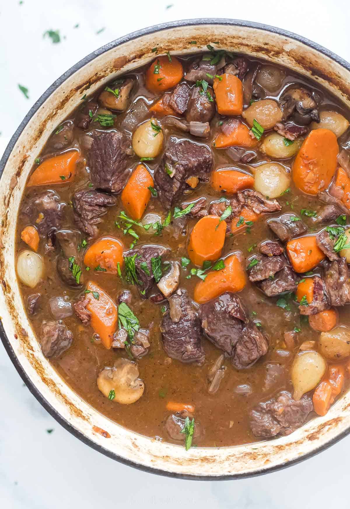 a pot of beef bourguignon with carrots, pearl onions, and mushrooms in a dark gravy